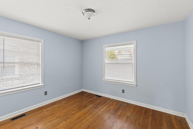 unfurnished room with hardwood / wood-style floors, baseboards, and visible vents