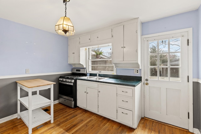 kitchen with a sink, white cabinets, stainless steel gas stove, dark countertops, and light wood-type flooring