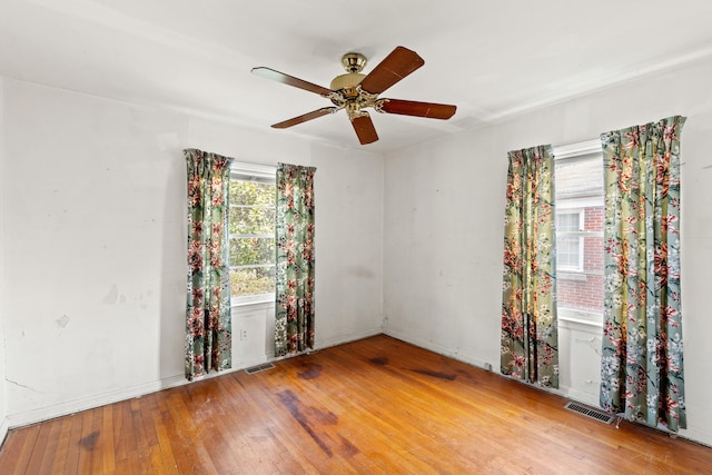 empty room with a wealth of natural light, visible vents, wood-type flooring, and a ceiling fan