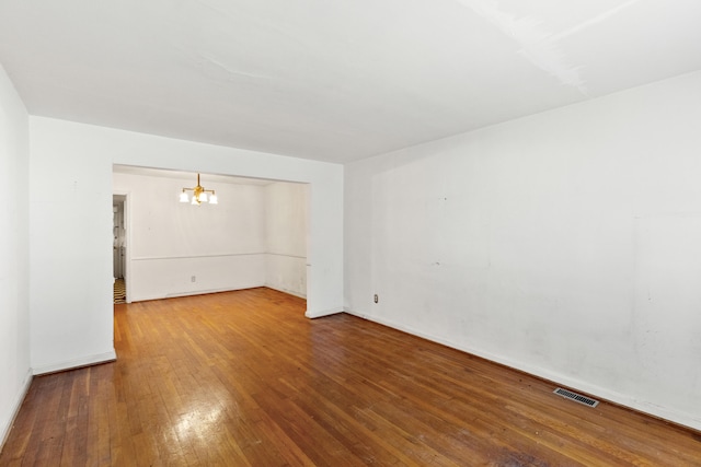 unfurnished room featuring visible vents, baseboards, an inviting chandelier, and hardwood / wood-style flooring