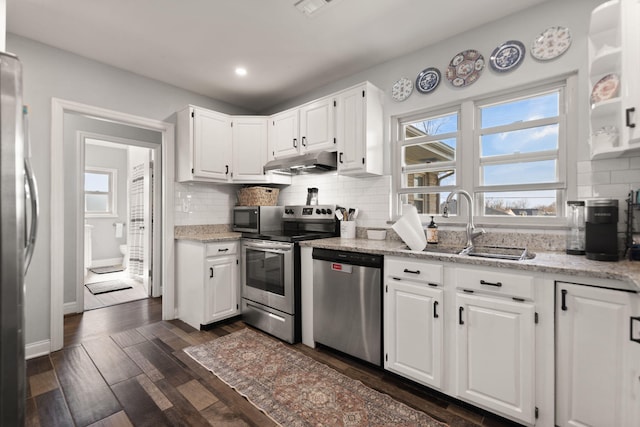 kitchen featuring tasteful backsplash, under cabinet range hood, white cabinets, stainless steel appliances, and dark wood-style flooring