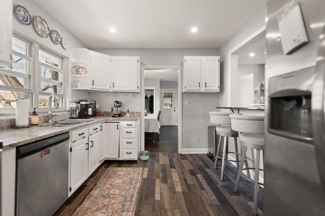 kitchen with a sink, backsplash, dark wood finished floors, stainless steel appliances, and white cabinets