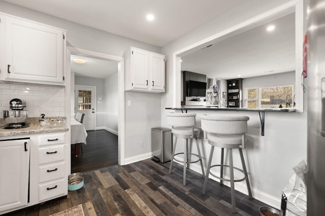 kitchen with dark wood-type flooring, baseboards, a breakfast bar, decorative backsplash, and white cabinets