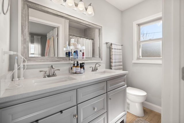 full bathroom with double vanity, toilet, baseboards, and a sink