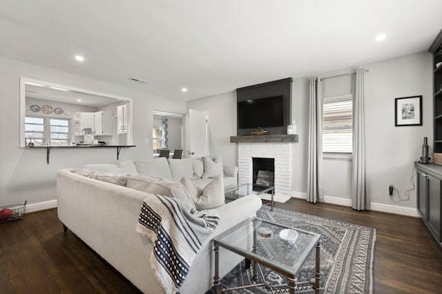 living room featuring dark wood-style floors, visible vents, a fireplace, and baseboards