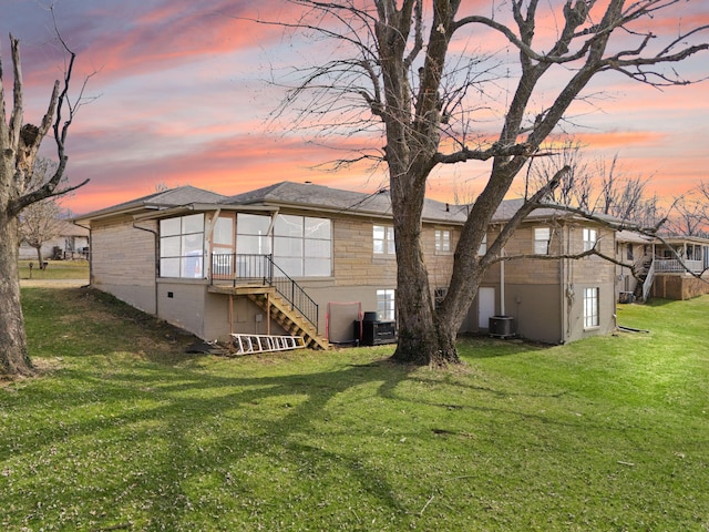 back of house at dusk with central AC unit, a lawn, and stairs