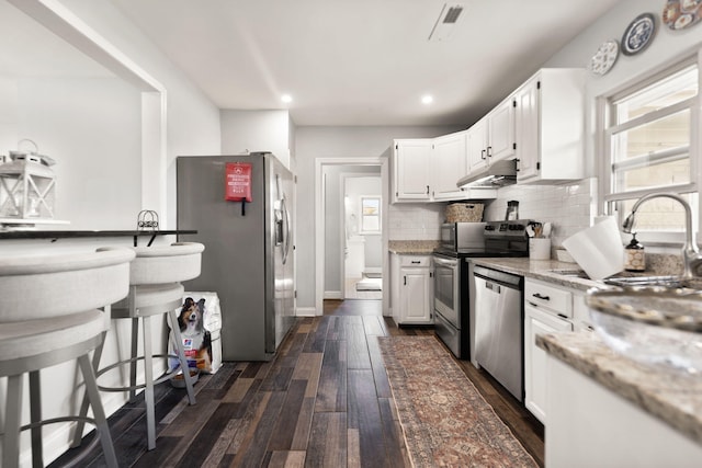 kitchen featuring dark wood-style flooring, stainless steel appliances, under cabinet range hood, white cabinetry, and tasteful backsplash