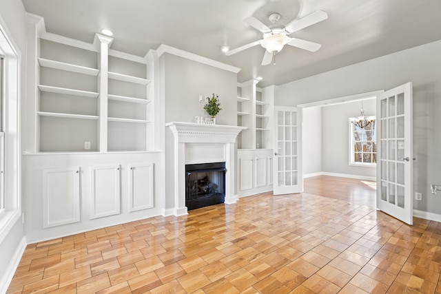 unfurnished living room featuring french doors, light wood-style flooring, built in features, and ceiling fan with notable chandelier