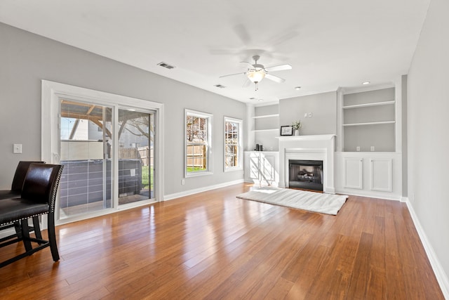 living room with a ceiling fan, visible vents, a glass covered fireplace, wood-type flooring, and baseboards