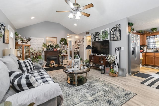 living area with light wood finished floors, a warm lit fireplace, a ceiling fan, and vaulted ceiling