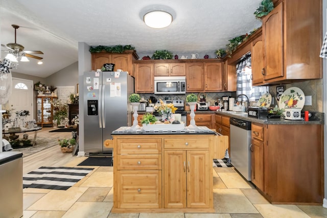 kitchen with a ceiling fan, a kitchen island, a sink, stainless steel appliances, and tasteful backsplash