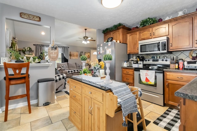 kitchen featuring a ceiling fan, tasteful backsplash, dark countertops, a kitchen island, and stainless steel appliances