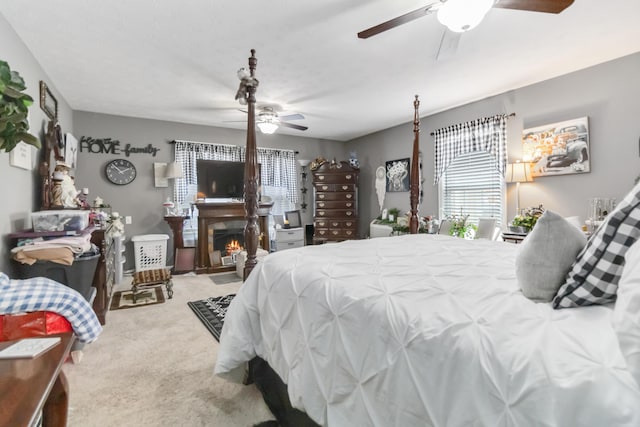 carpeted bedroom featuring multiple windows, a ceiling fan, and a lit fireplace