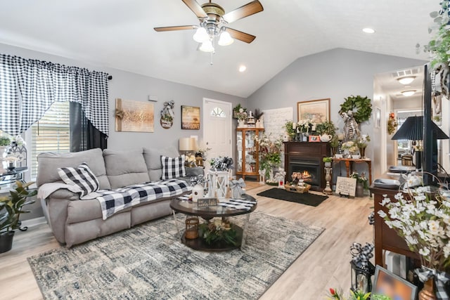 living room with visible vents, a warm lit fireplace, wood finished floors, lofted ceiling, and ceiling fan