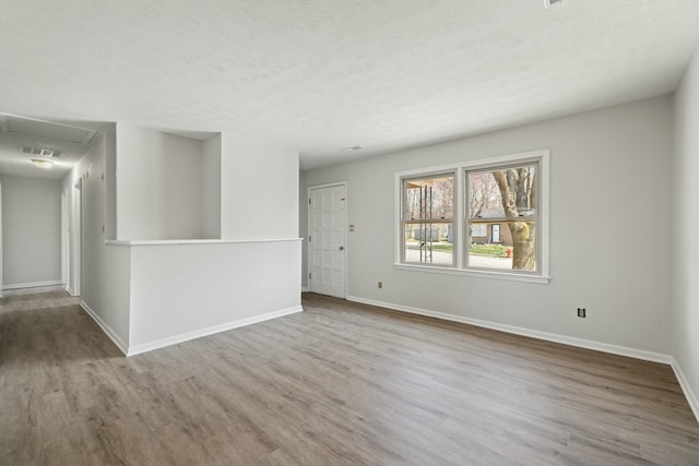 empty room featuring attic access, wood finished floors, baseboards, and a textured ceiling