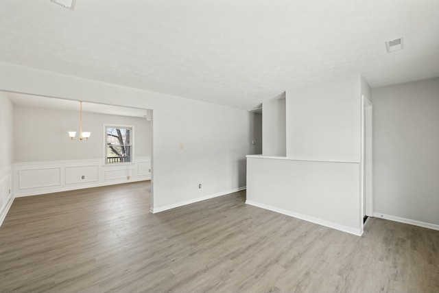 spare room with a chandelier, visible vents, baseboards, and wood finished floors