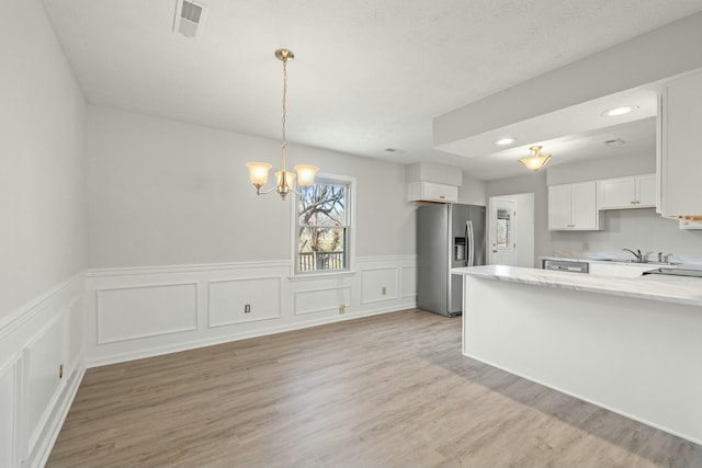 kitchen with a chandelier, light wood-style flooring, white cabinets, stainless steel fridge, and a sink