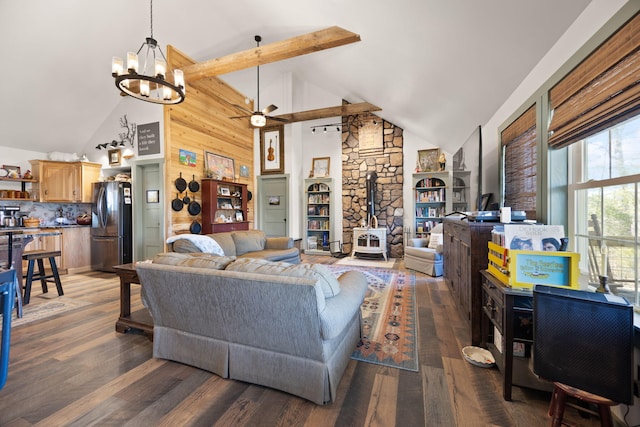 living area featuring ceiling fan with notable chandelier, high vaulted ceiling, a wood stove, and wood finished floors