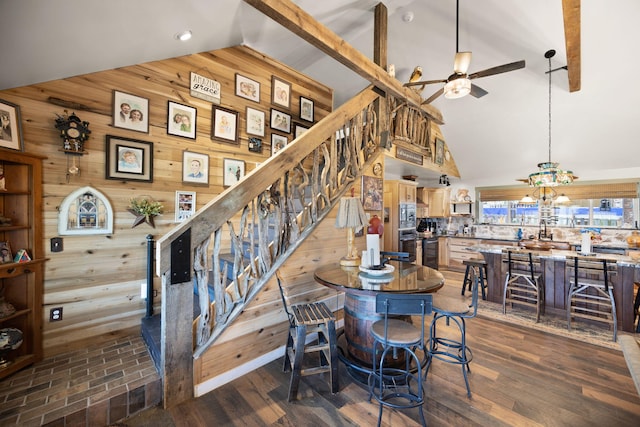 dining room featuring stairway, ceiling fan with notable chandelier, dark wood-style flooring, and wood walls