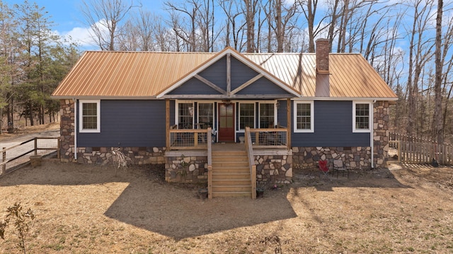 rustic home featuring a porch, fence, a chimney, and metal roof