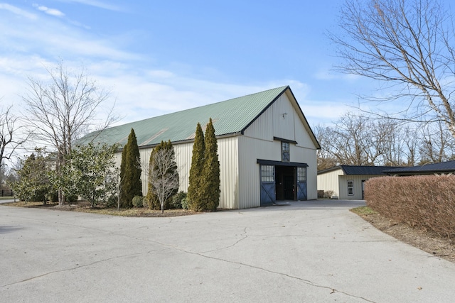 exterior space featuring concrete driveway, an outbuilding, and metal roof