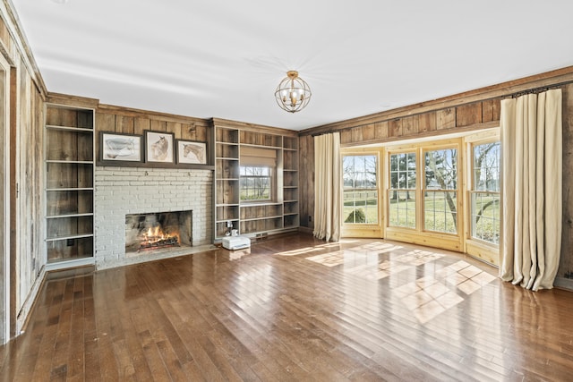 unfurnished living room featuring built in features, an inviting chandelier, a fireplace, dark wood-style flooring, and wood walls