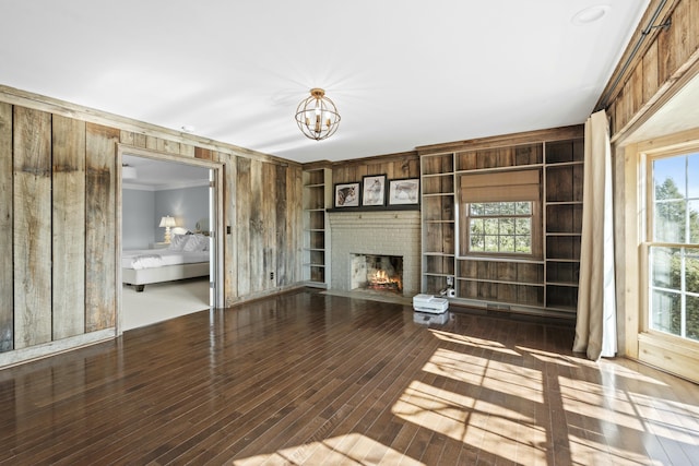 unfurnished living room with a notable chandelier, built in features, wood-type flooring, wooden walls, and a fireplace