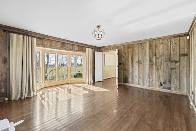 unfurnished room featuring an inviting chandelier, wooden walls, and wood finished floors