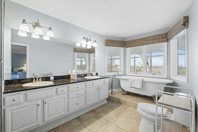 full bath with a sink, a freestanding bath, double vanity, and tile patterned floors