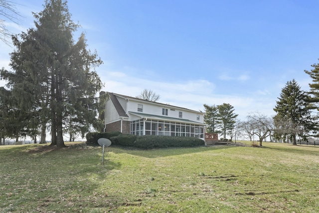 rear view of house featuring brick siding, a lawn, and a sunroom