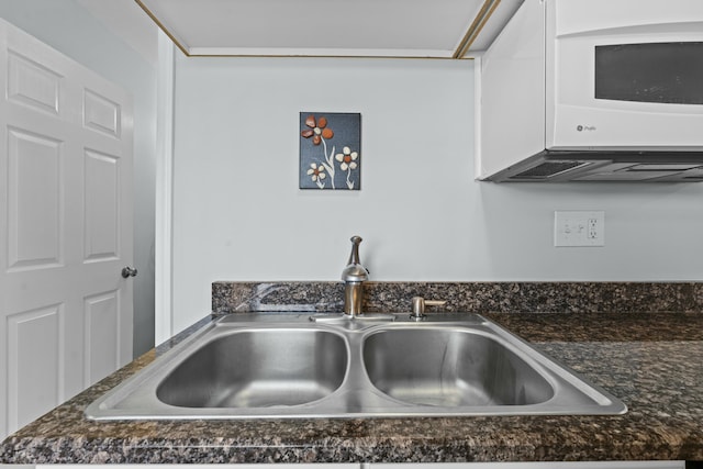 room details featuring white cabinets, dark stone counters, and a sink