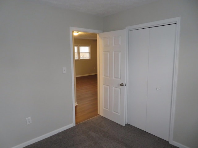 unfurnished bedroom featuring dark colored carpet, a closet, and baseboards