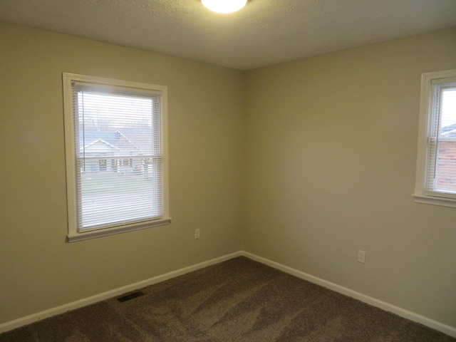 spare room with visible vents, baseboards, and dark carpet