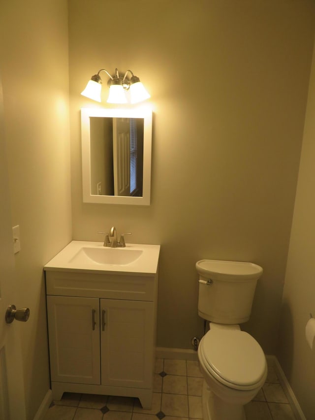 half bathroom with vanity, tile patterned floors, toilet, and baseboards