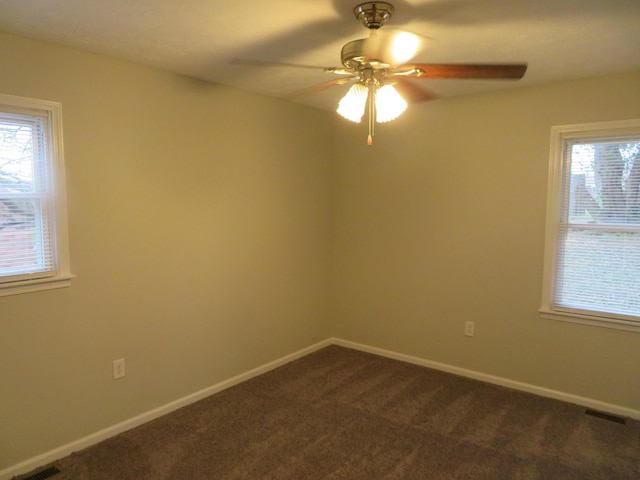 spare room with dark colored carpet, visible vents, baseboards, and ceiling fan