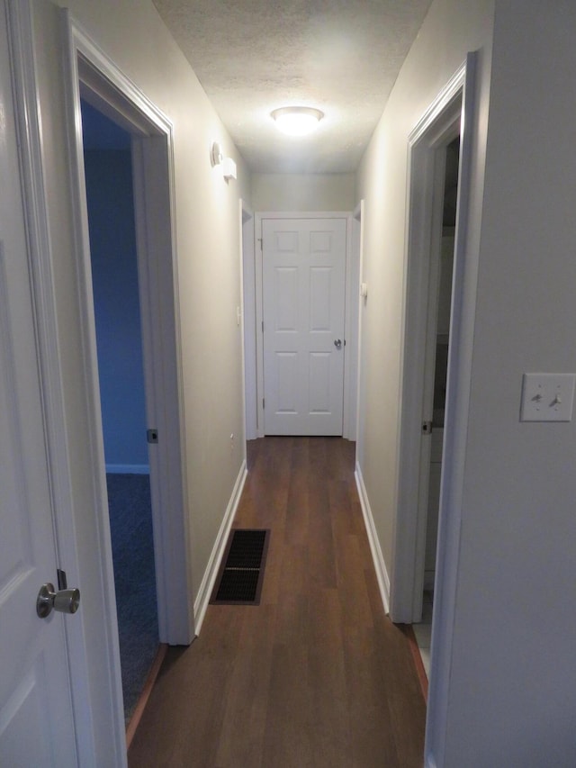 hall with visible vents, a textured ceiling, baseboards, and wood finished floors