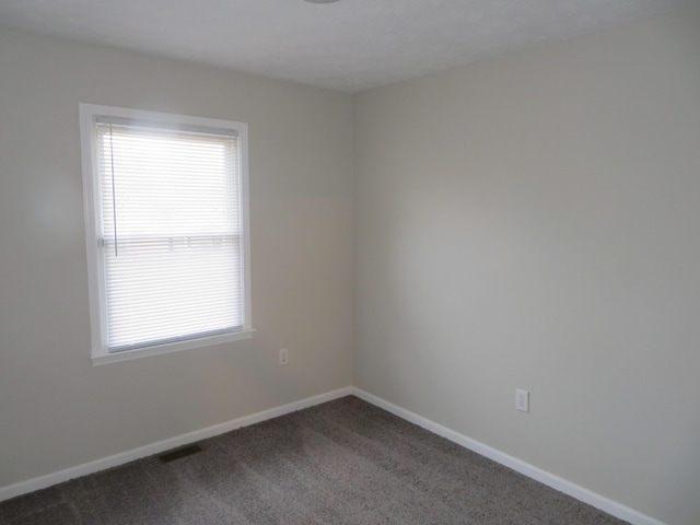 unfurnished room with visible vents, dark carpet, and baseboards