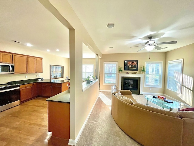 kitchen featuring brown cabinetry, appliances with stainless steel finishes, a glass covered fireplace, dark countertops, and open floor plan