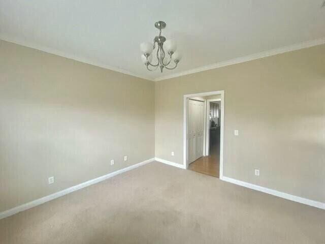 carpeted empty room with baseboards, a notable chandelier, and crown molding