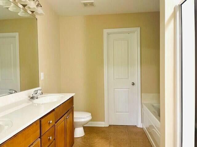 bathroom featuring visible vents, double vanity, a sink, tile patterned flooring, and a bath