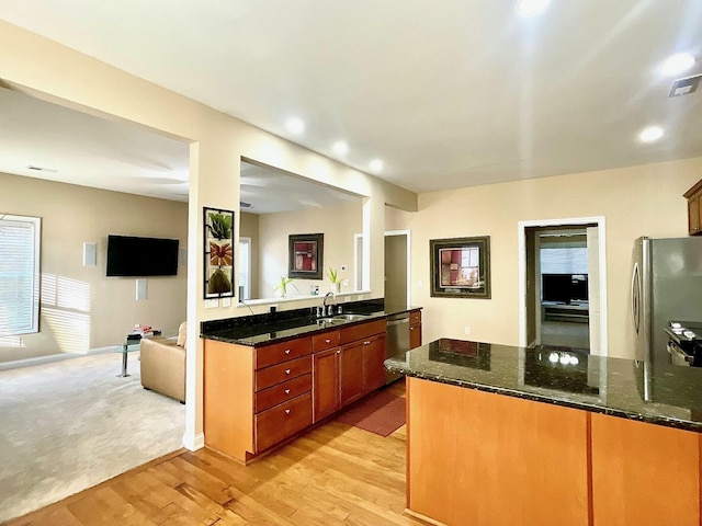 kitchen with a sink, stainless steel appliances, light wood-type flooring, and dark stone countertops