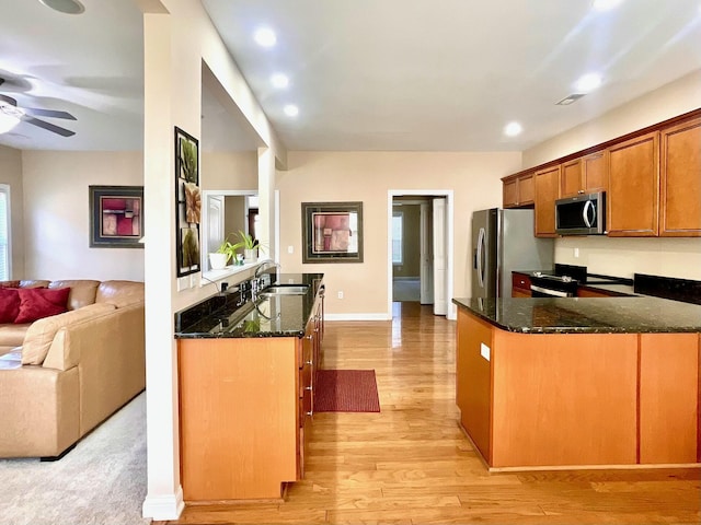 kitchen featuring light wood finished floors, dark stone counters, a sink, appliances with stainless steel finishes, and open floor plan