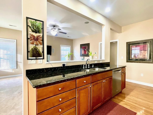 kitchen featuring dark stone countertops, stainless steel dishwasher, brown cabinets, and a sink