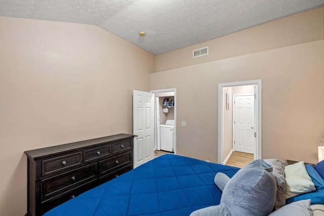 bedroom featuring visible vents, light wood finished floors, washer / dryer, vaulted ceiling, and a textured ceiling