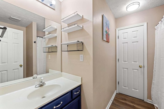 full bath with visible vents, a textured ceiling, wood finished floors, baseboards, and vanity