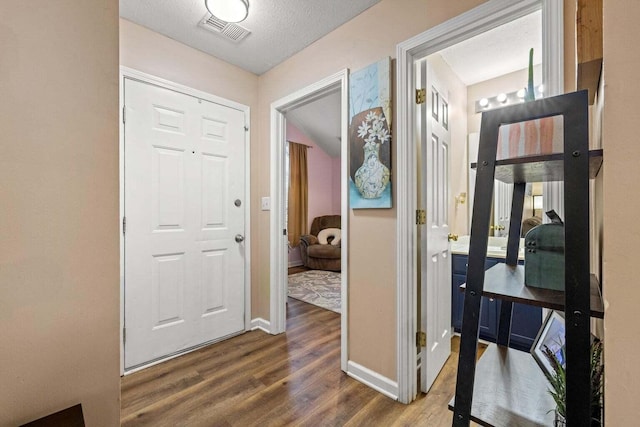 hallway featuring visible vents, baseboards, a textured ceiling, and wood finished floors