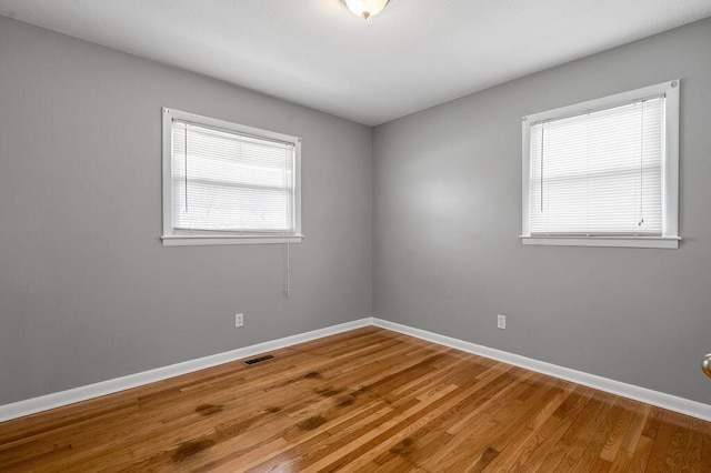 empty room featuring wood finished floors, visible vents, and baseboards