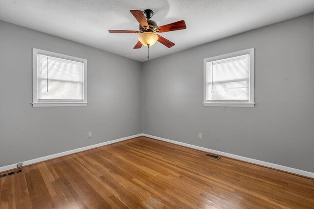 empty room featuring ceiling fan, visible vents, baseboards, and hardwood / wood-style floors