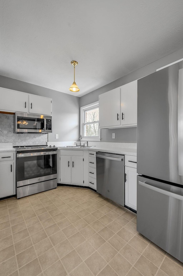 kitchen with appliances with stainless steel finishes, white cabinetry, light countertops, and a sink
