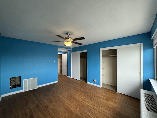 unfurnished bedroom with visible vents, two closets, a ceiling fan, wood finished floors, and baseboards